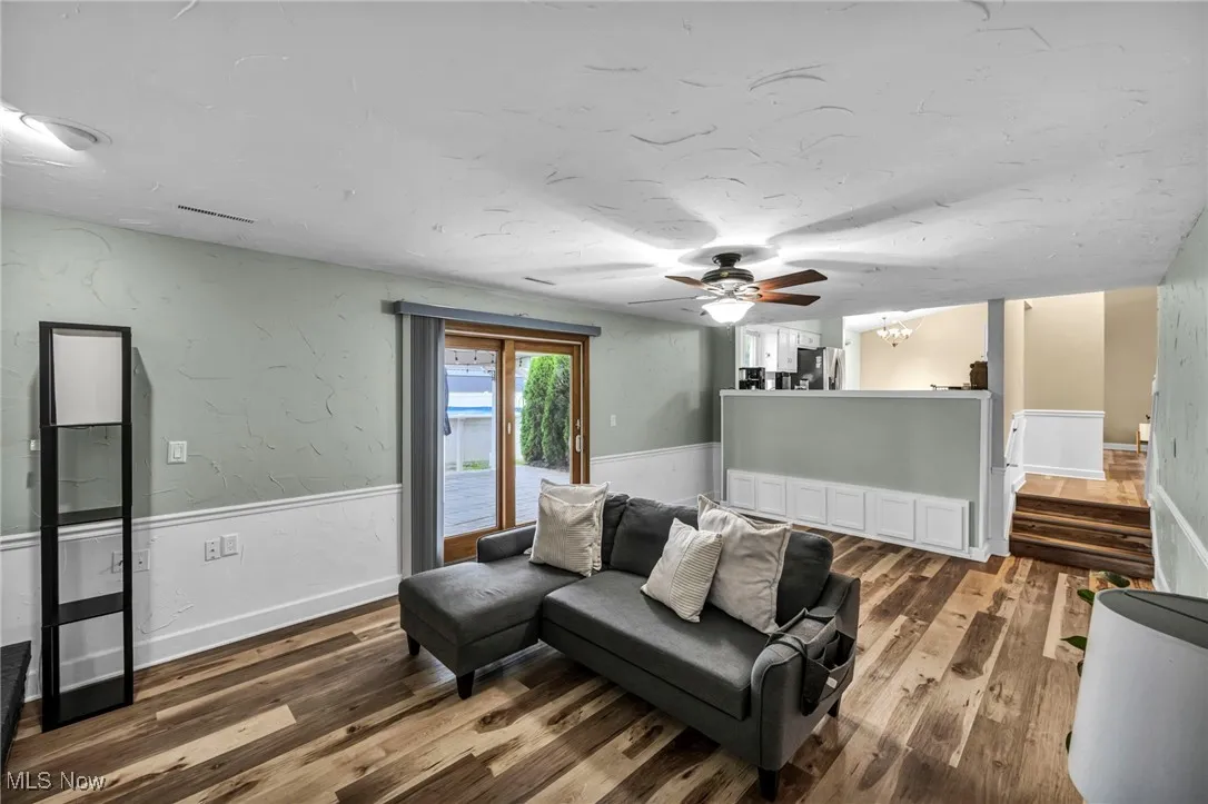 Living room with a textured wall, dark wood finished floors, ceiling fan, stairs, and a wainscoted wall