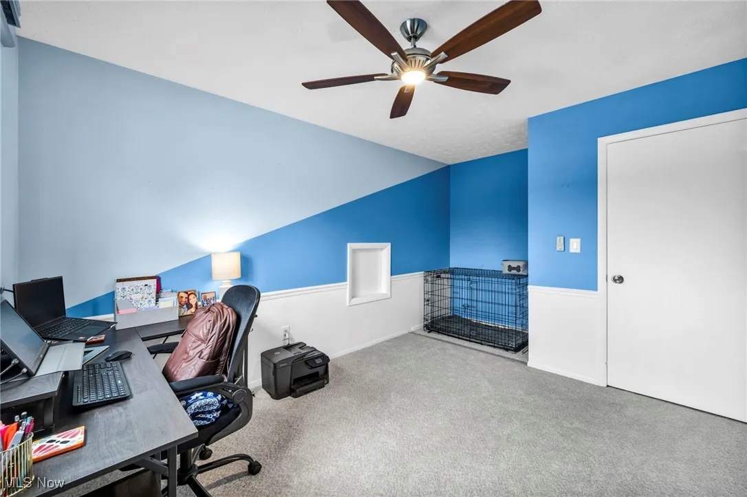 Carpeted home office featuring ceiling fan and baseboards