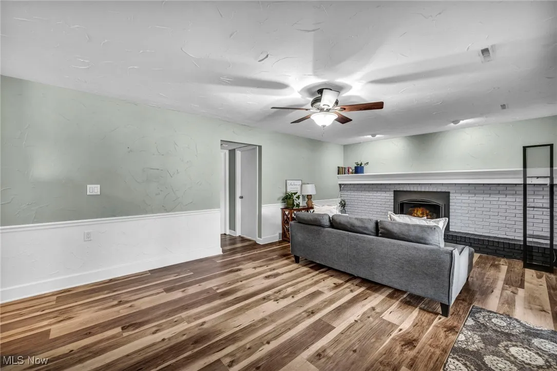 Living area featuring a textured wall, a fireplace, ceiling fan, and wood finished floors