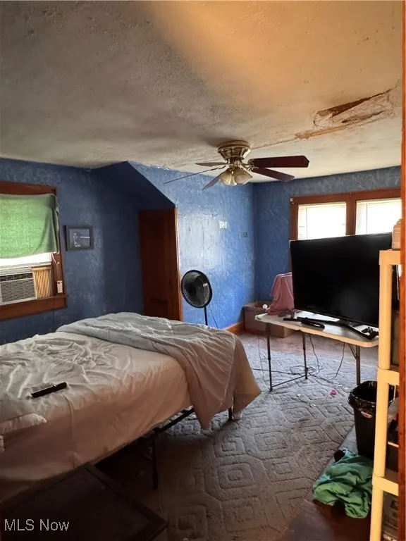 Bedroom featuring a textured wall, a textured ceiling, a ceiling fan, and cooling unit