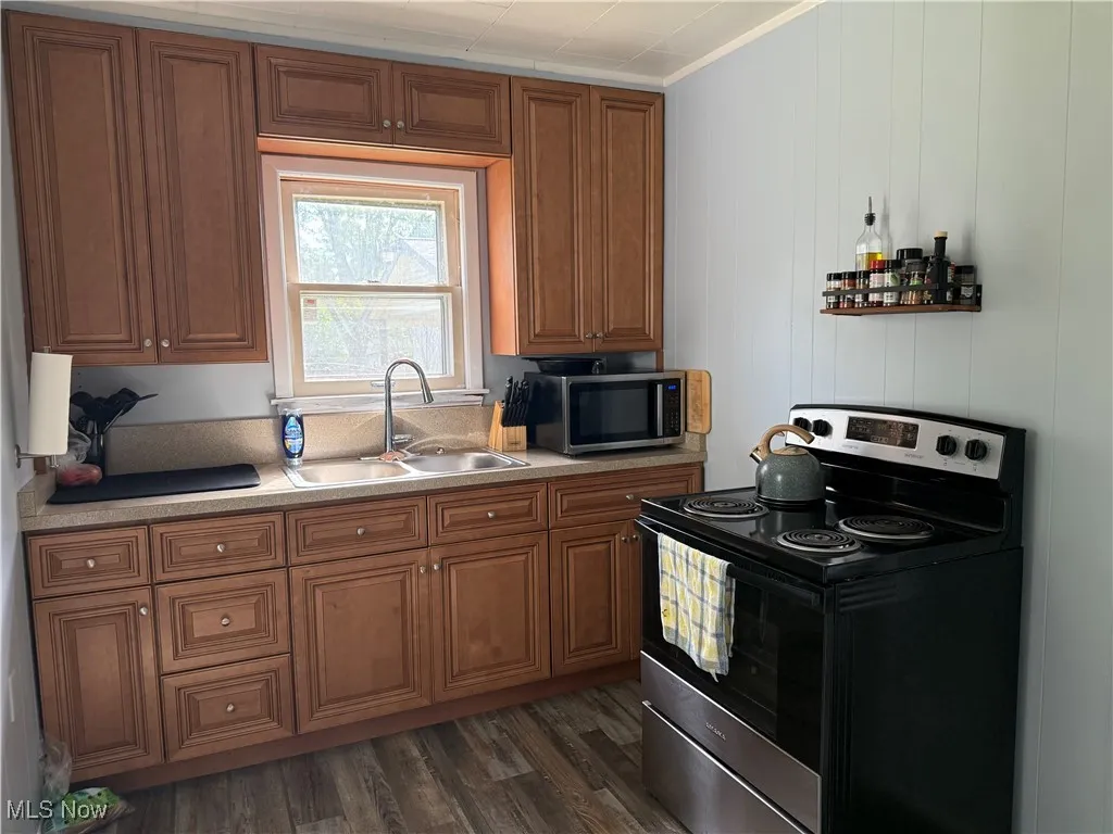 Kitchen featuring appliances with stainless steel finishes, dark wood finished floors, brown cabinets, light countertops, and ornamental molding