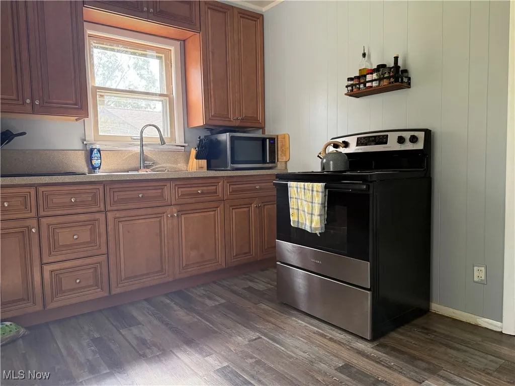 Kitchen featuring appliances with stainless steel finishes, dark wood-style flooring, light stone counters, and brown cabinets