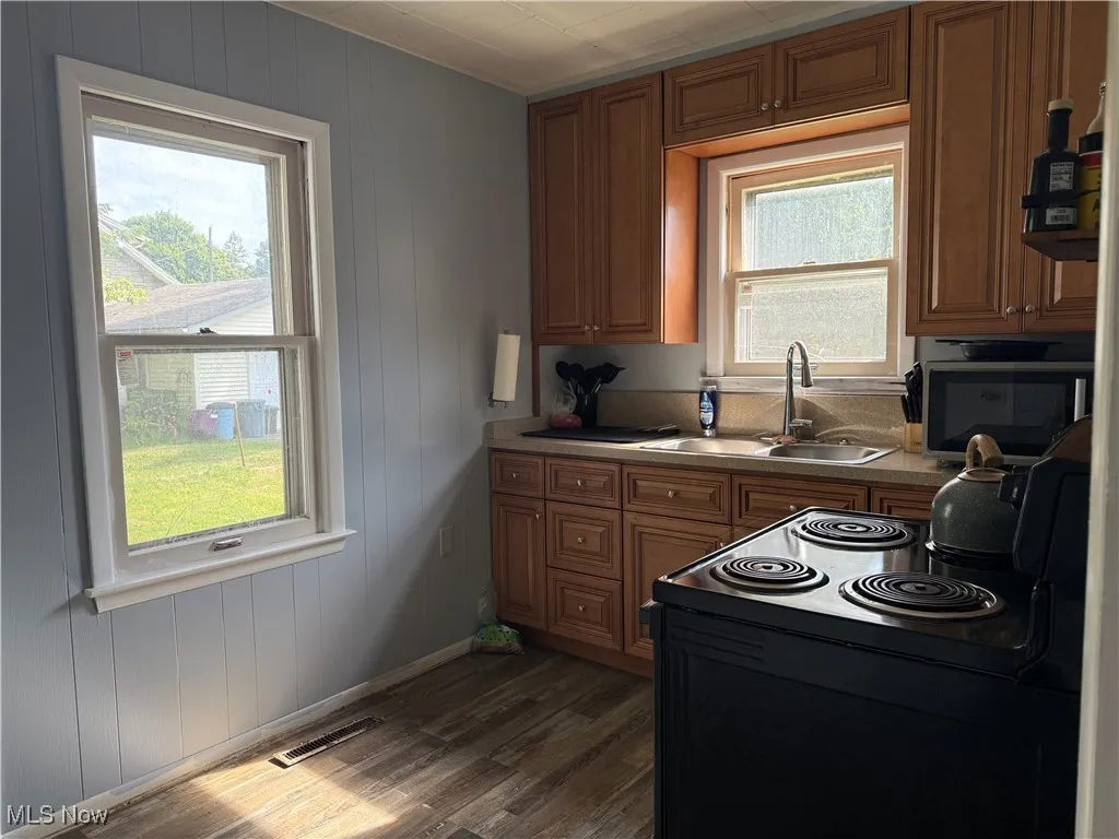 Kitchen featuring black electric range oven, wooden walls, brown cabinetry, dark wood-style flooring, and light countertops