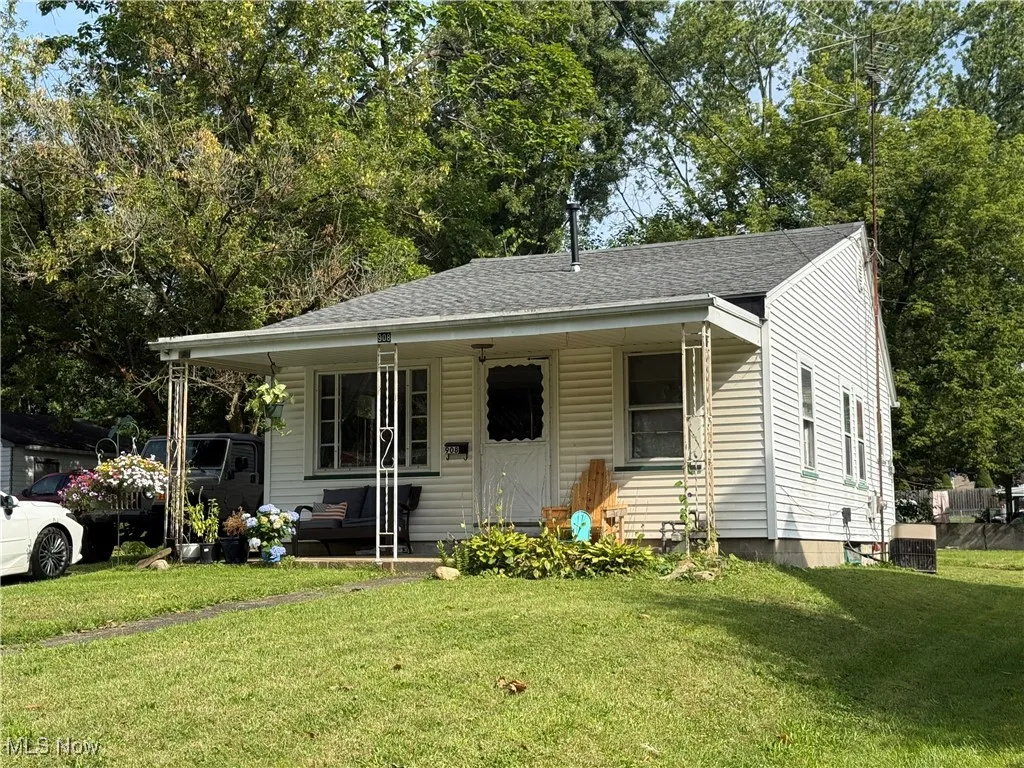 Bungalow featuring roof with shingles, a front yard, and view of wooded area