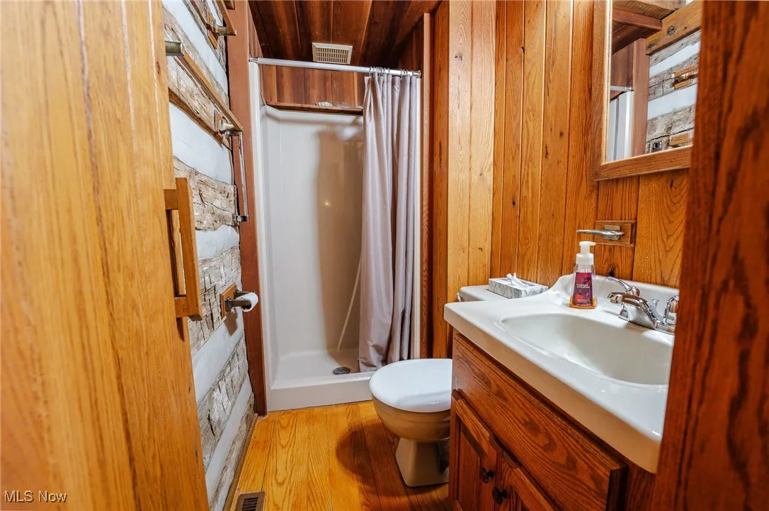 Full bath with a stall shower, light wood-type flooring, vanity, and wooden walls