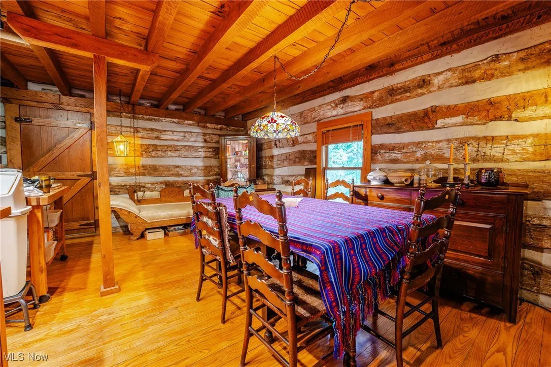 Dining space with light wood-style floors, wood walls, and a wooden ceiling with exposed beams