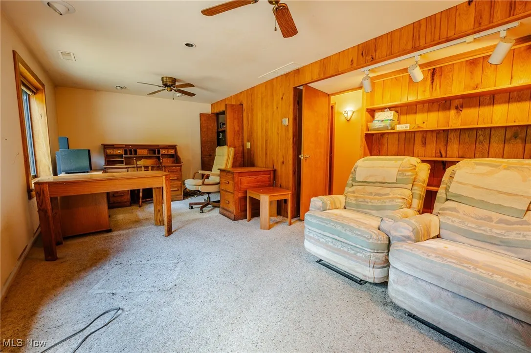 Living room featuring wood walls, an office area, and a ceiling fan