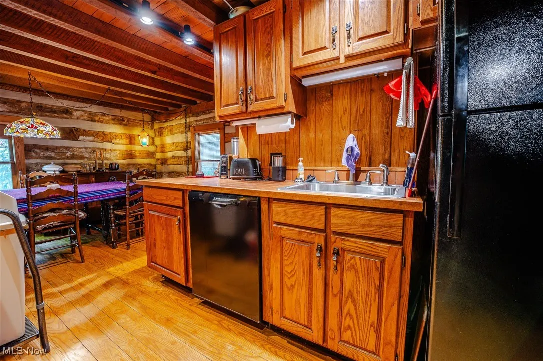 Kitchen featuring black appliances, brown cabinetry, wooden walls, hanging light fixtures, and light wood-type flooring