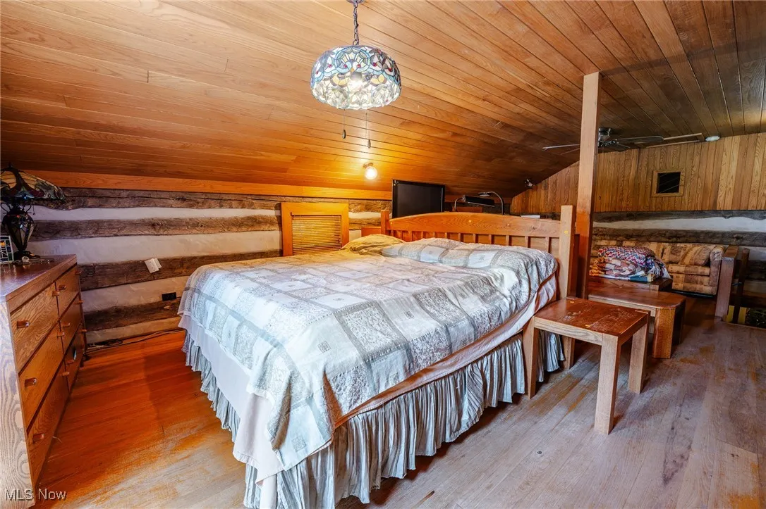 Bedroom with wooden ceiling, lofted ceiling, light wood-style floors, and wooden walls