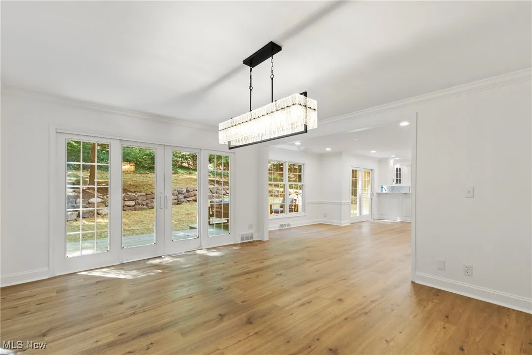 Unfurnished living room featuring ornamental molding, light wood finished floors, and a chandelier