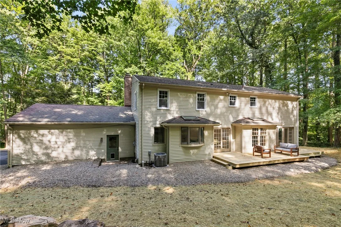 Back of property with a chimney, a wooden deck, and view of scattered trees