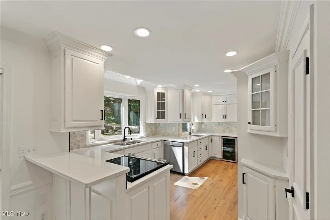 Kitchen featuring glass insert cabinets, white cabinetry, light wood-style floors, black electric cooktop, and decorative backsplash