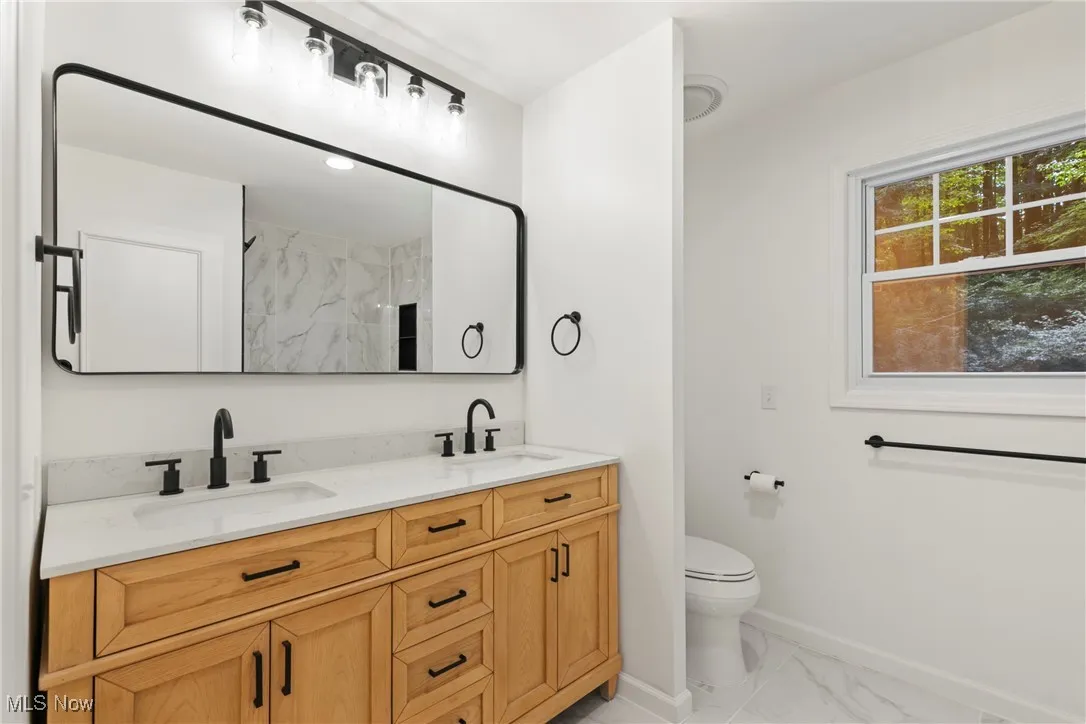 Bathroom featuring double vanity, light marble finish floors, and a marble finish shower