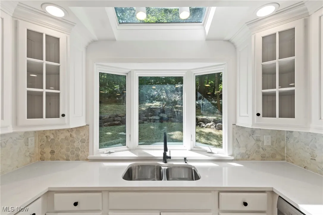 Kitchen with glass insert cabinets, tasteful backsplash, white cabinetry, and light stone counters