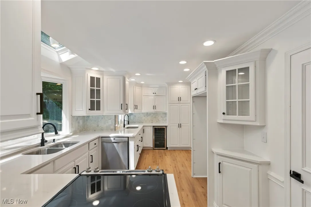 Kitchen with glass insert cabinets, white cabinetry, light wood finished floors, light stone counters, and recessed lighting