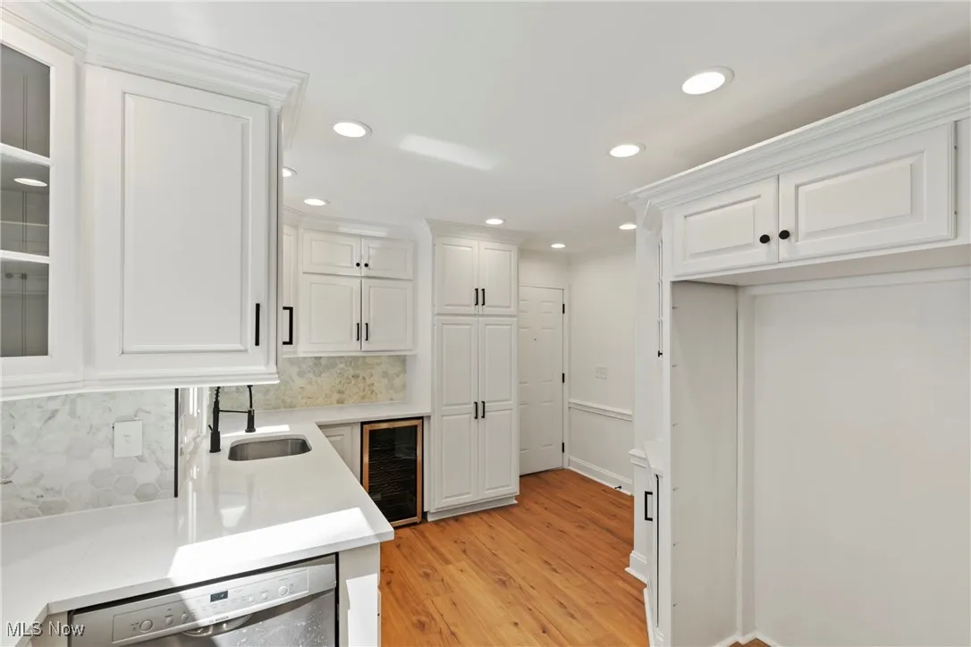 Kitchen featuring recessed lighting, white cabinets, stainless steel dishwasher, wine cooler, and light wood finished floors