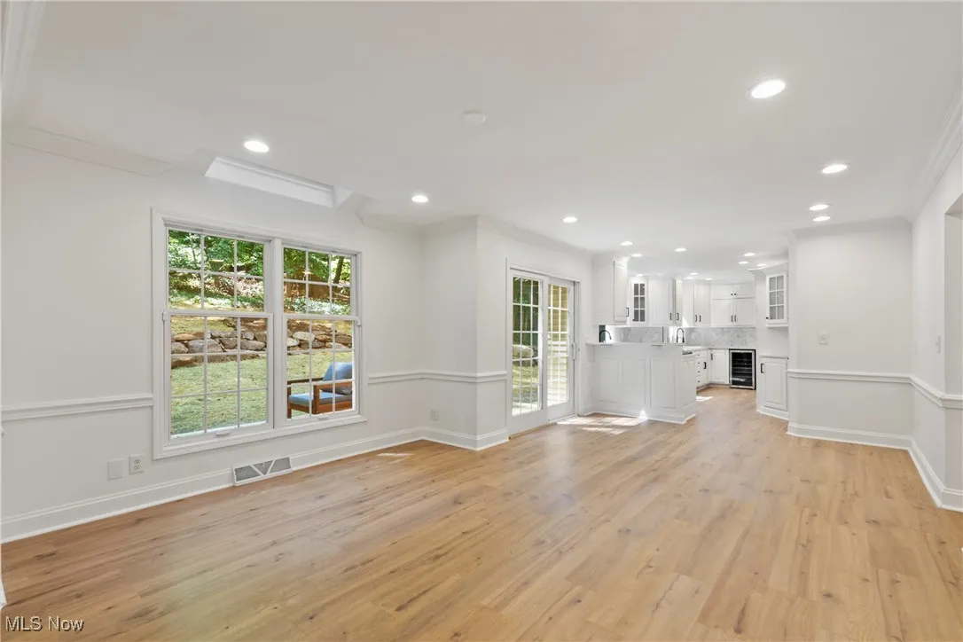 Unfurnished living room with ornamental molding, light wood-type flooring, recessed lighting, and beverage cooler