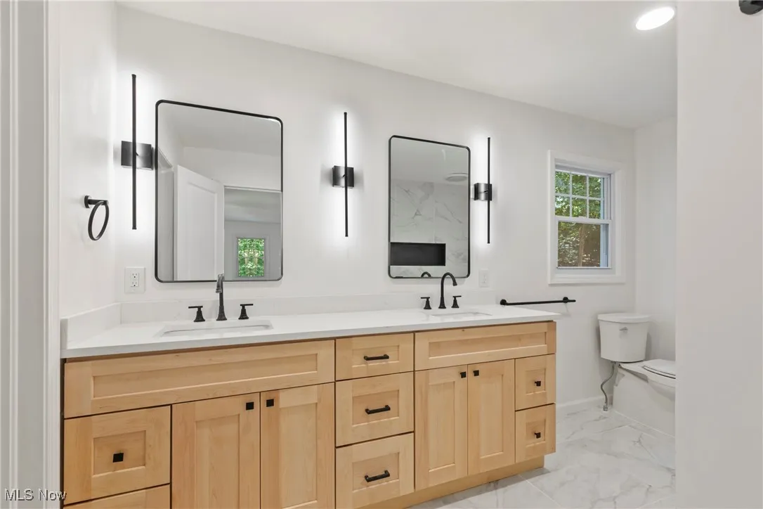 Bathroom with double vanity, light marble finish flooring, and recessed lighting