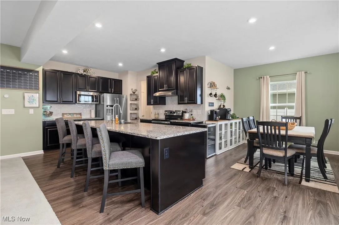 Kitchen featuring dark wood-type flooring, recessed lighting, stainless steel appliances, an island with sink, and backsplash
