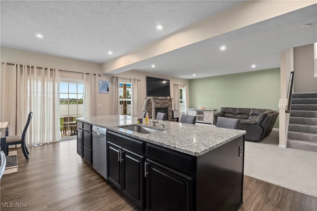 Kitchen featuring dark cabinets, a textured ceiling, a stone fireplace, light stone counters, and recessed lighting