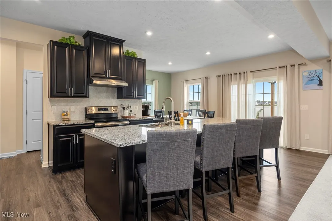 Kitchen featuring light stone counters, recessed lighting, electric range, dark wood-style flooring, and an island with sink
