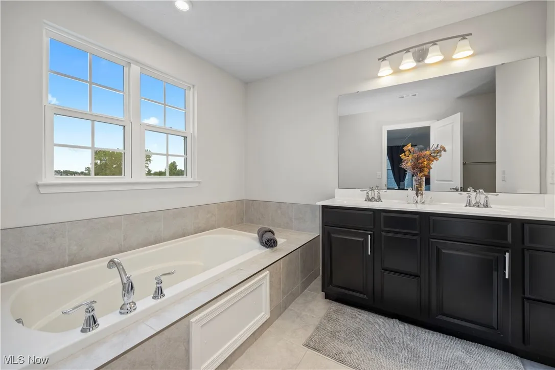 Full bath featuring double vanity, a bath, light tile patterned floors, and recessed lighting