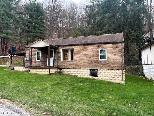 View of front of house featuring a chimney, a front lawn, a porch, and view of scattered trees