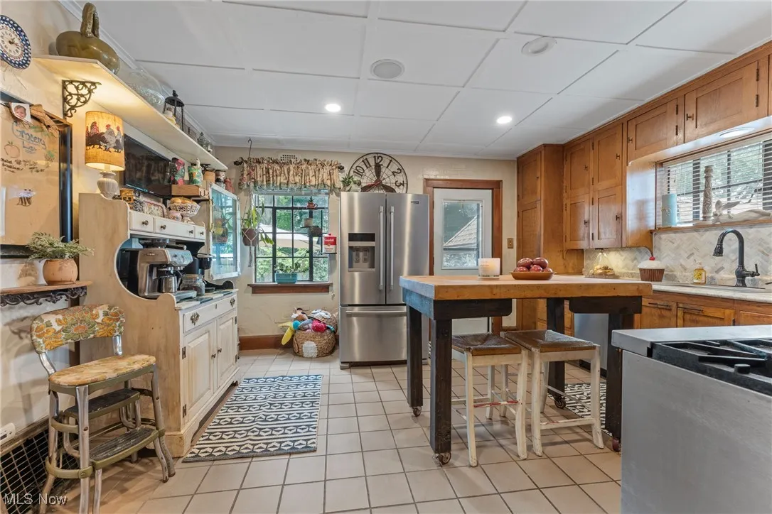 Kitchen with stainless steel fridge, light tile patterned flooring, light countertops, recessed lighting, and brown cabinetry