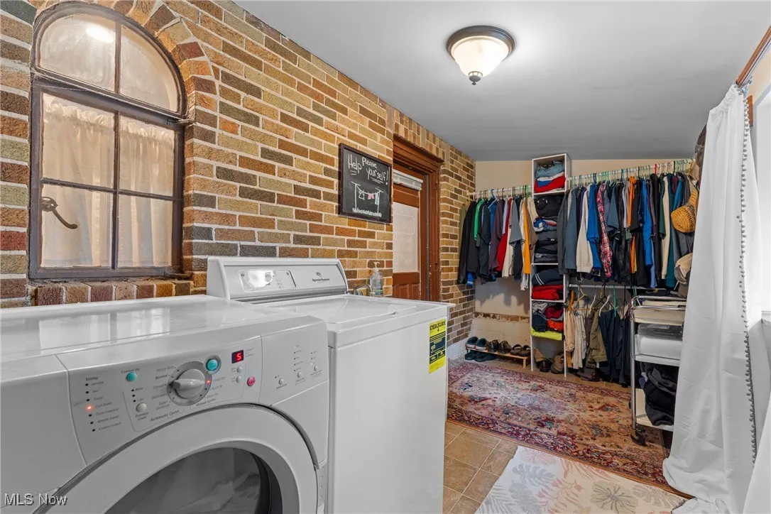 Laundry area featuring brick wall, light tile patterned flooring, and independent washer and dryer