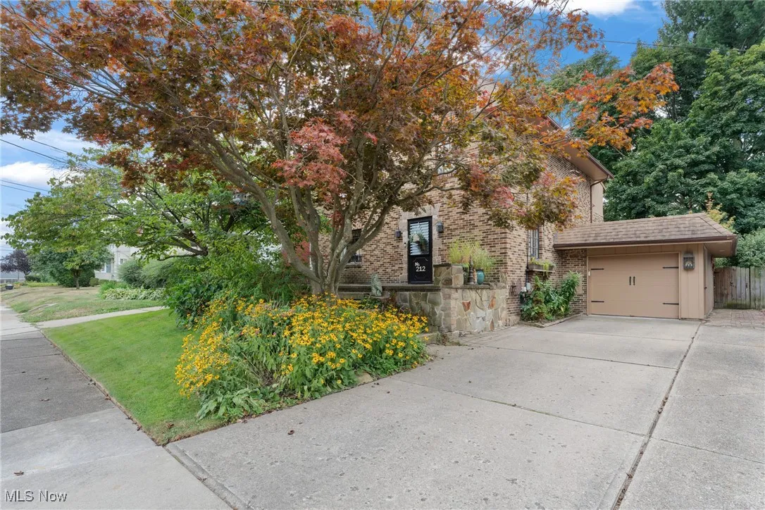 View of property hidden behind natural elements featuring a garage, concrete driveway, brick siding, and stone siding