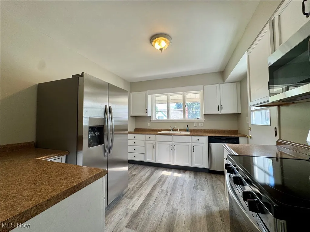 Kitchen with appliances with stainless steel finishes, dark countertops, white cabinets, and light wood finished floors