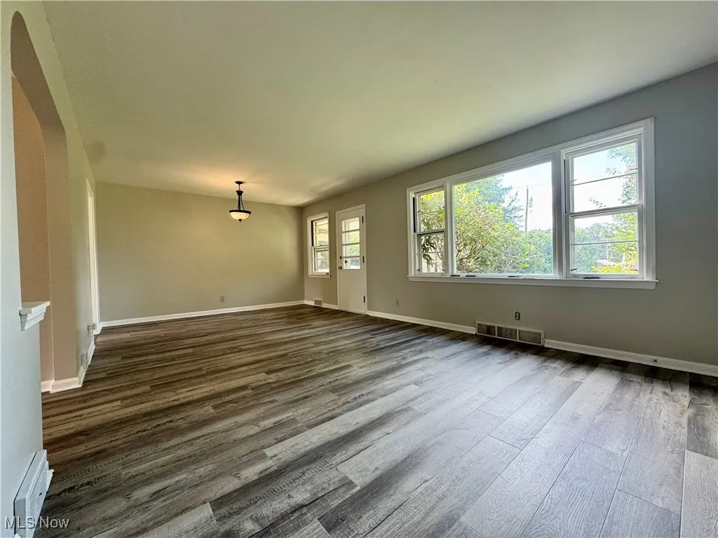 Unfurnished living room with wood finished floors, a baseboard heating unit, and arched walkways