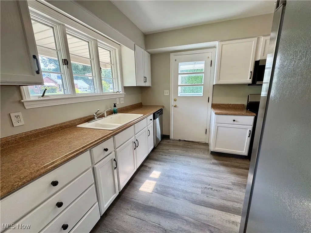 Kitchen featuring appliances with stainless steel finishes, white cabinets, light wood finished floors, and dark countertops