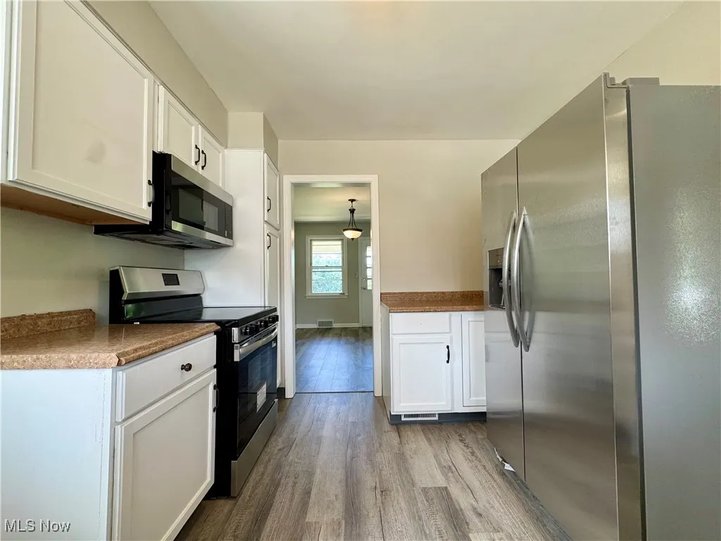 Kitchen with stainless steel appliances, white cabinets, dark wood finished floors, decorative light fixtures, and dark countertops