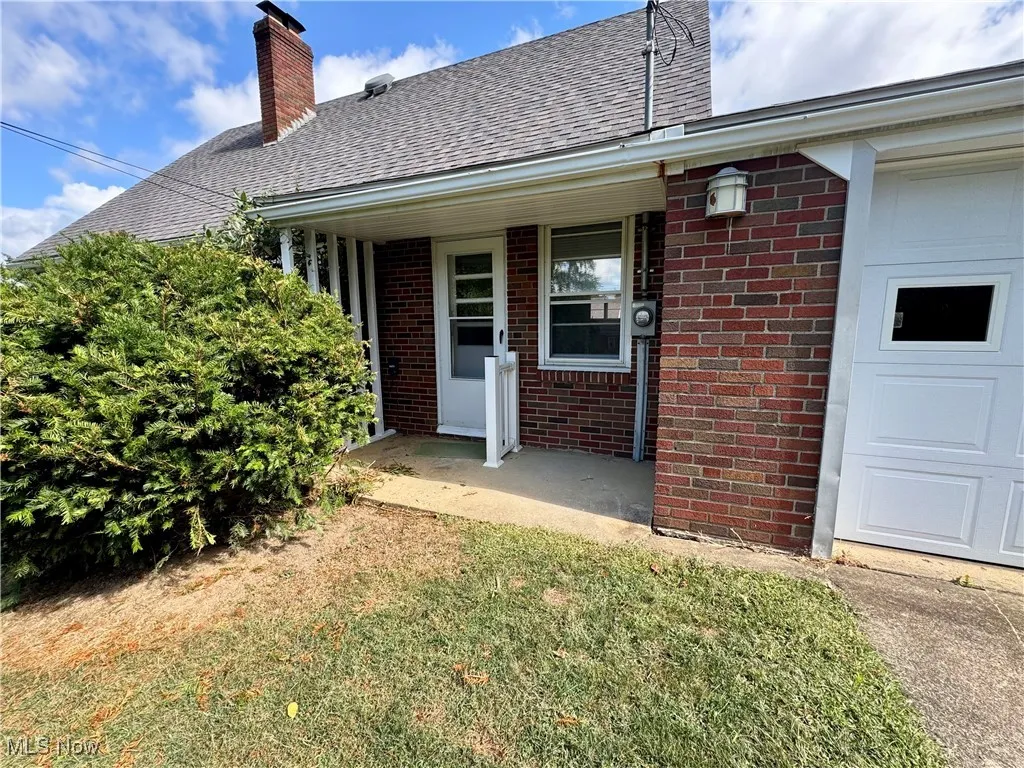 Property entrance with brick siding, a chimney, roof with shingles, a patio, and a lawn