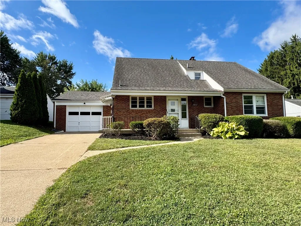 View of front of house featuring a front lawn, roof with shingles, driveway, brick siding, and an attached garage