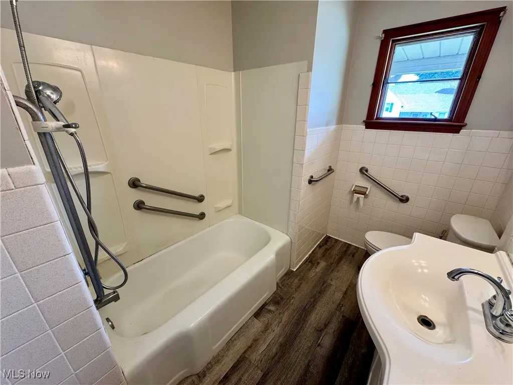 Bathroom with dark wood-style flooring, tile walls, wainscoting, and tub / shower combination