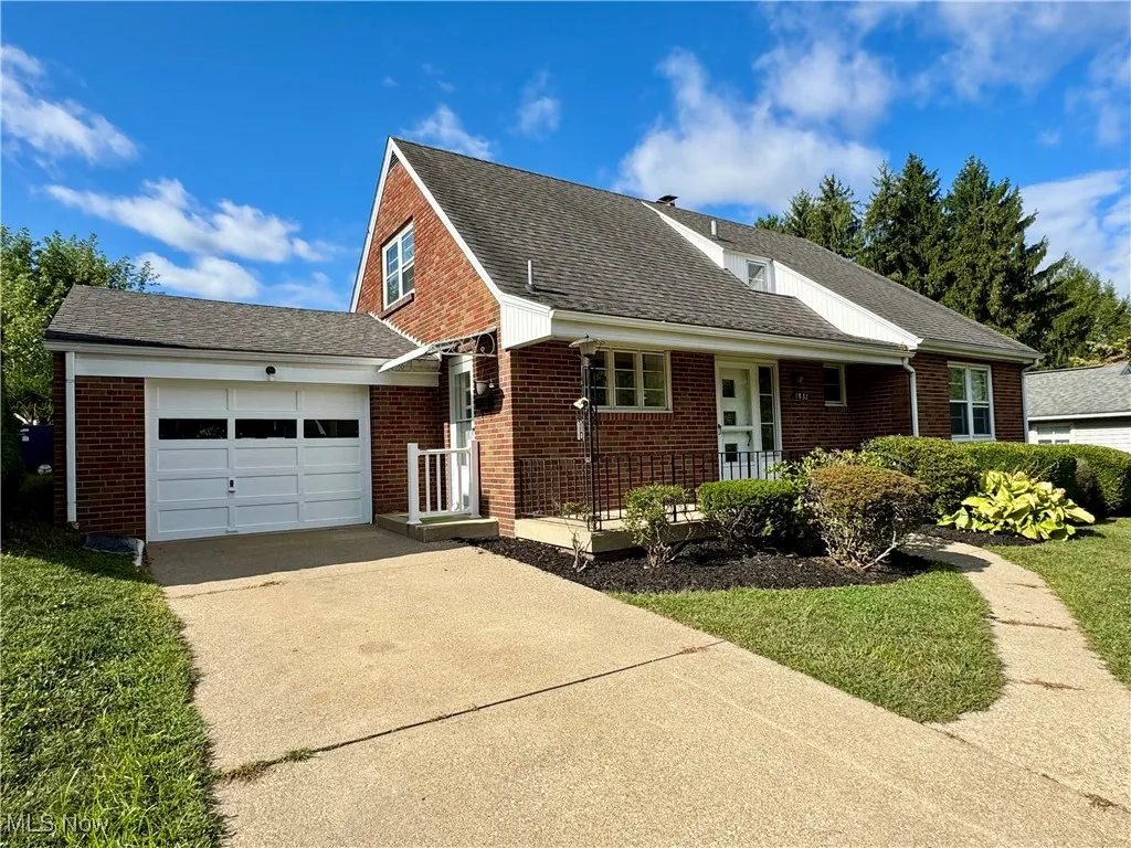 View of front of home featuring an attached garage, roof with shingles, concrete driveway, brick siding, and a front yard