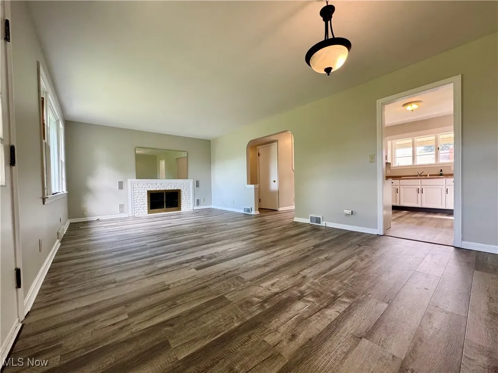Unfurnished living room with dark wood finished floors, arched walkways, and a fireplace
