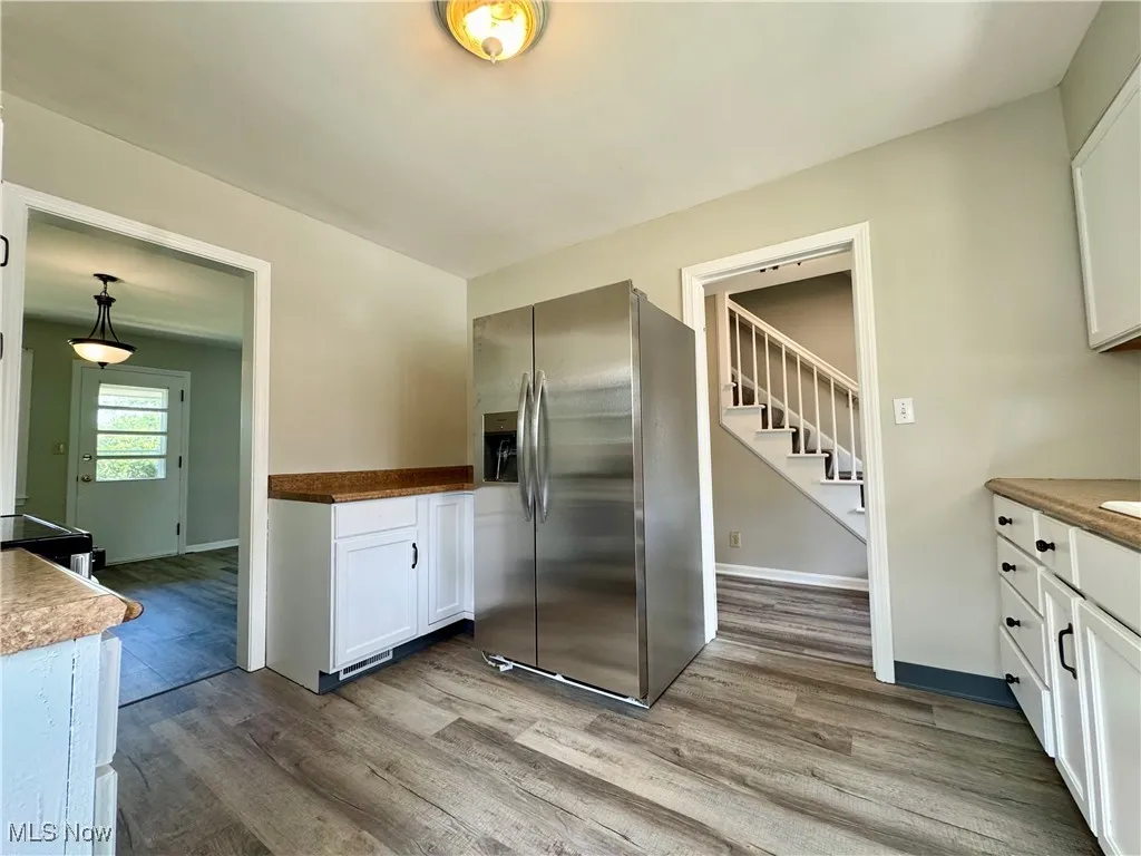 Kitchen featuring stainless steel fridge, white cabinets, light wood finished floors, and black range with electric cooktop