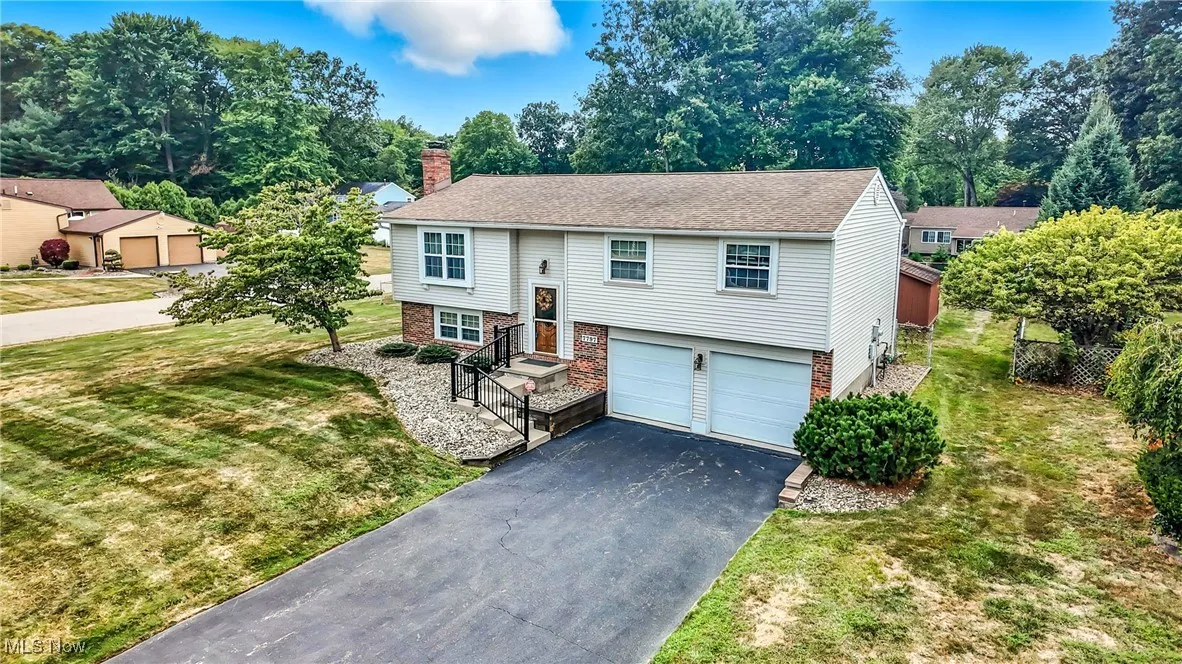 Split foyer home featuring brick siding, asphalt driveway, a chimney, a garage, and a front lawn