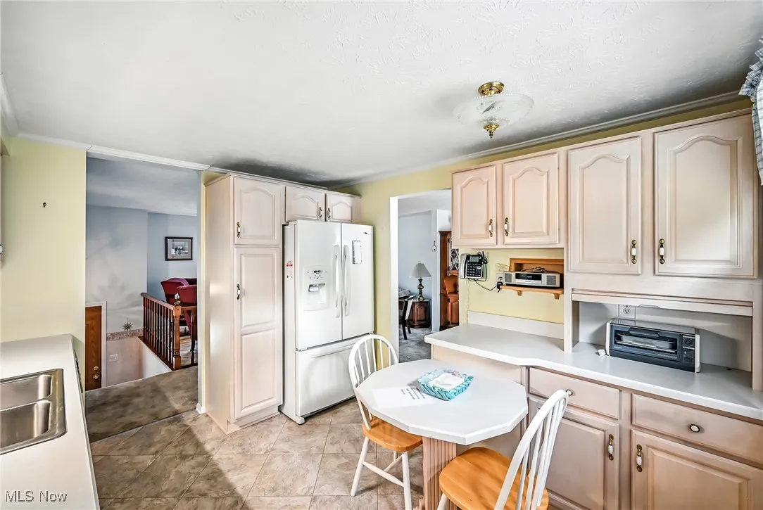 Kitchen with white refrigerator with ice dispenser, light countertops, light tile patterned floors, and a textured ceiling