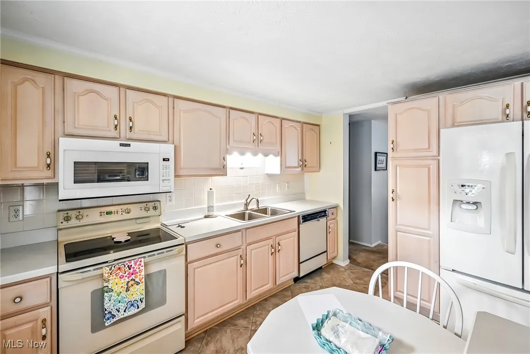 Kitchen with light brown cabinetry, white appliances, and light countertops