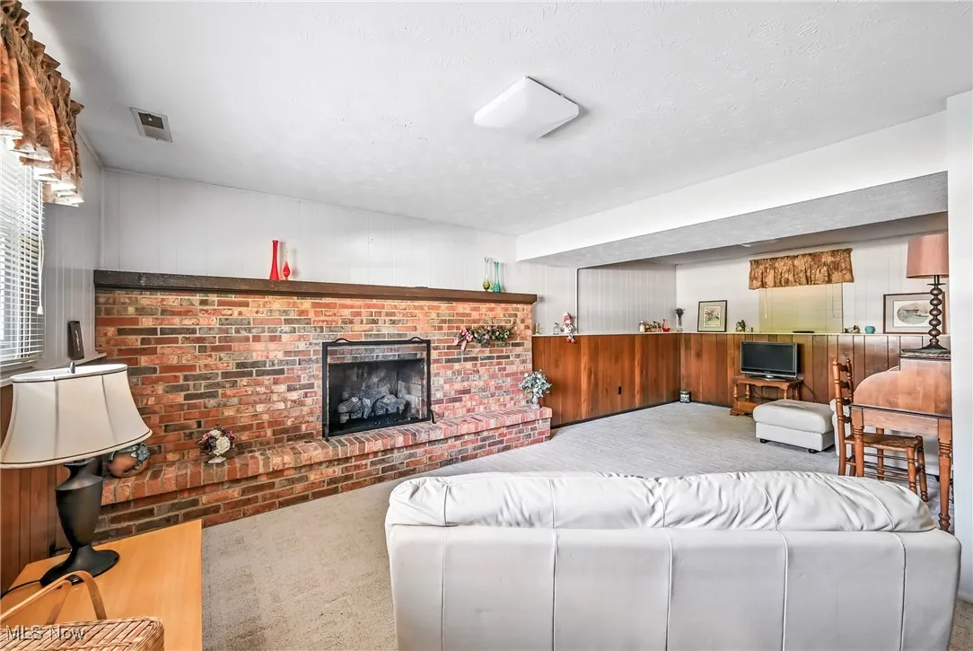 Carpeted living area featuring wooden walls, a brick fireplace, and a textured ceiling