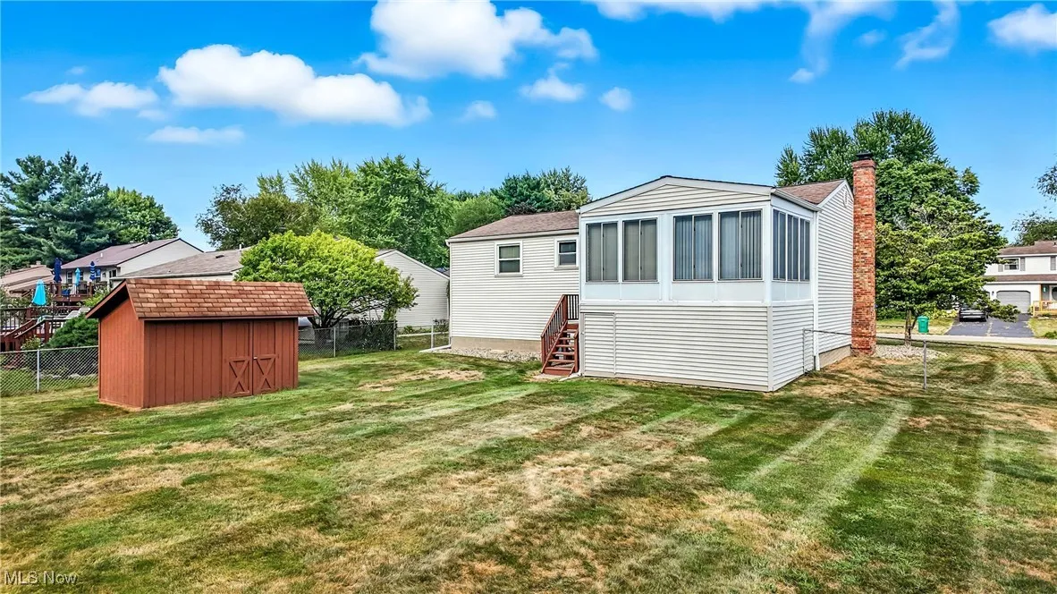 Rear view of house with a storage shed, a fenced backyard, a sunroom, and a chimney