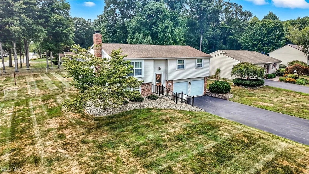 Raised ranch featuring brick siding, a chimney, driveway, a garage, and a front yard