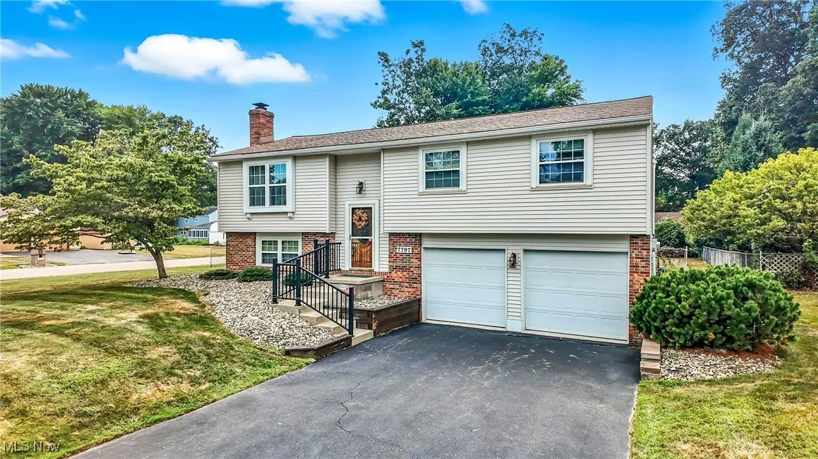 Bi-level home featuring brick siding, asphalt driveway, a front yard, a chimney, and a garage