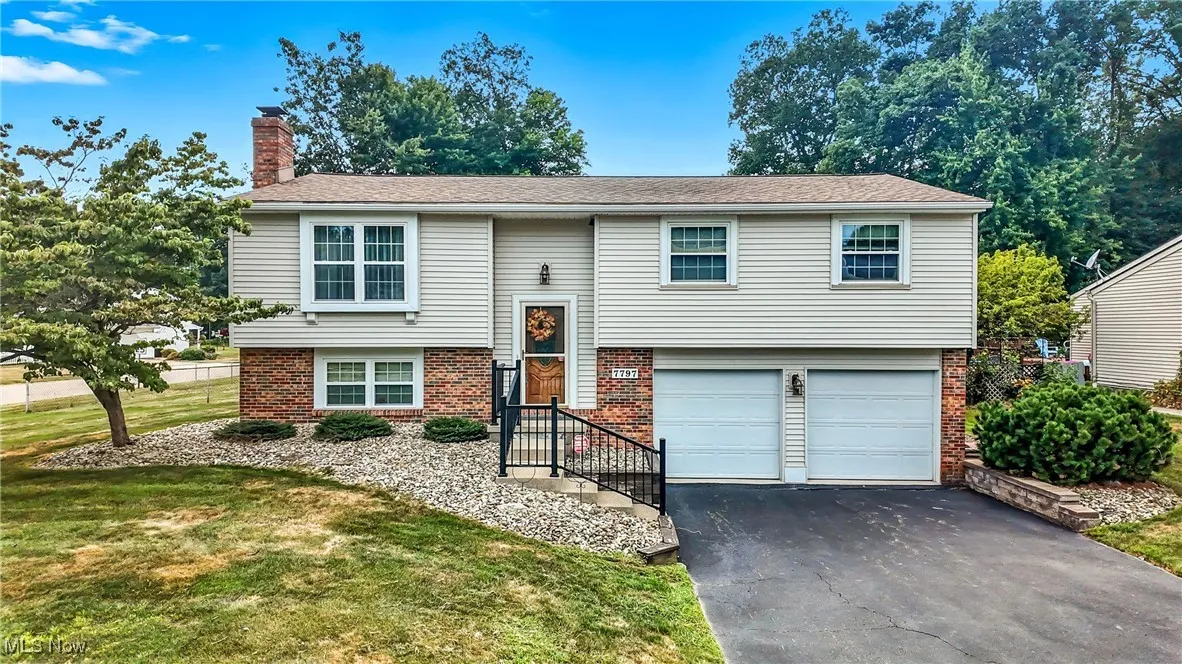 Split foyer home featuring brick siding, a chimney, asphalt driveway, and a front yard