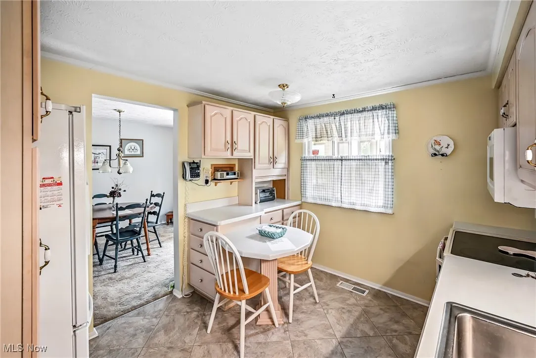 Kitchen featuring light brown cabinets, white appliances, a textured ceiling, a chandelier, and light countertops