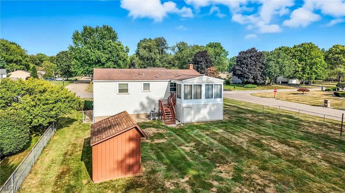 Back of property with a fenced backyard, a sunroom, view of scattered trees, stairway, and a storage unit
